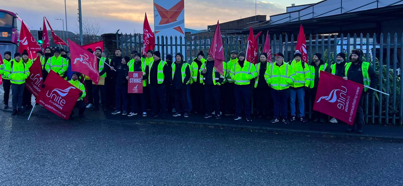 About 30 workers in hi-viz jackets holding Unite the union flags on strike in Belfast at an industrial park.