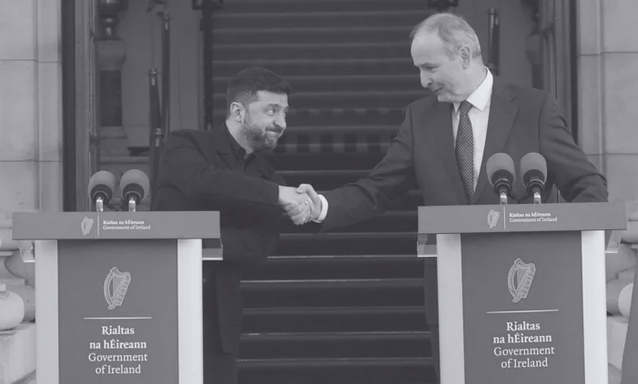 Zelensky leans over his podium to shake Martin's hand in front of government buildings.